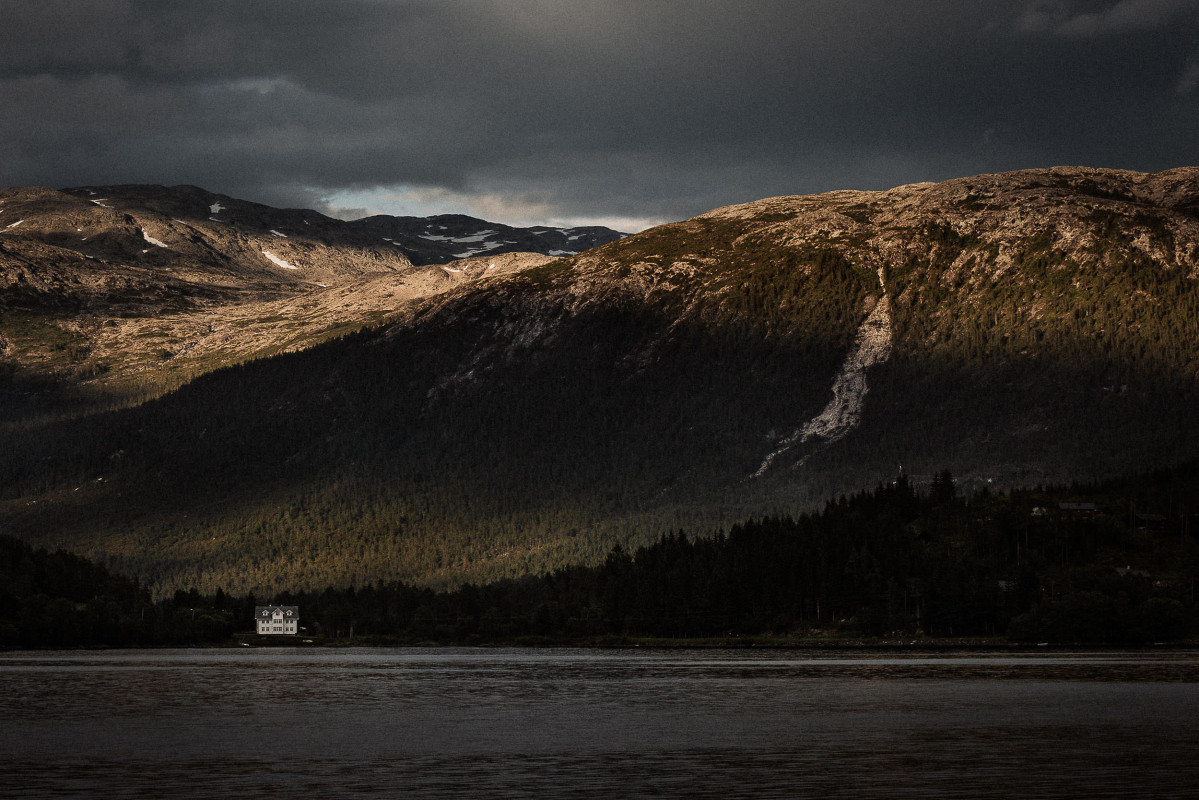 Einsames Haus im Fjord vor bewaldetem Berghang