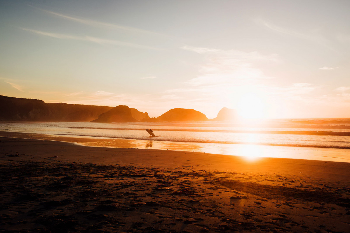 Surfer mit Longboard in der auslaufenden Brandung bei Sonnenuntergang